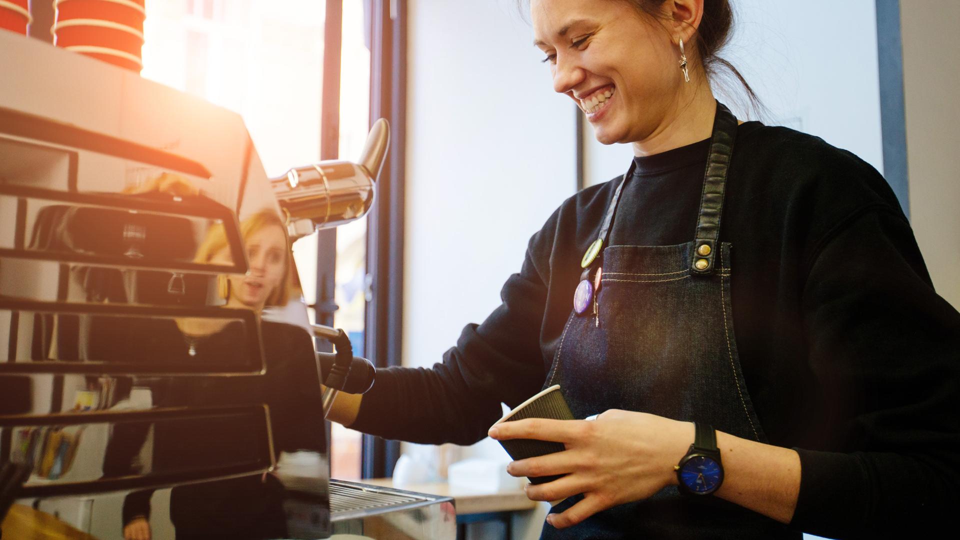 En kvinna ler och serverar kaffe i kassan på ett kafé