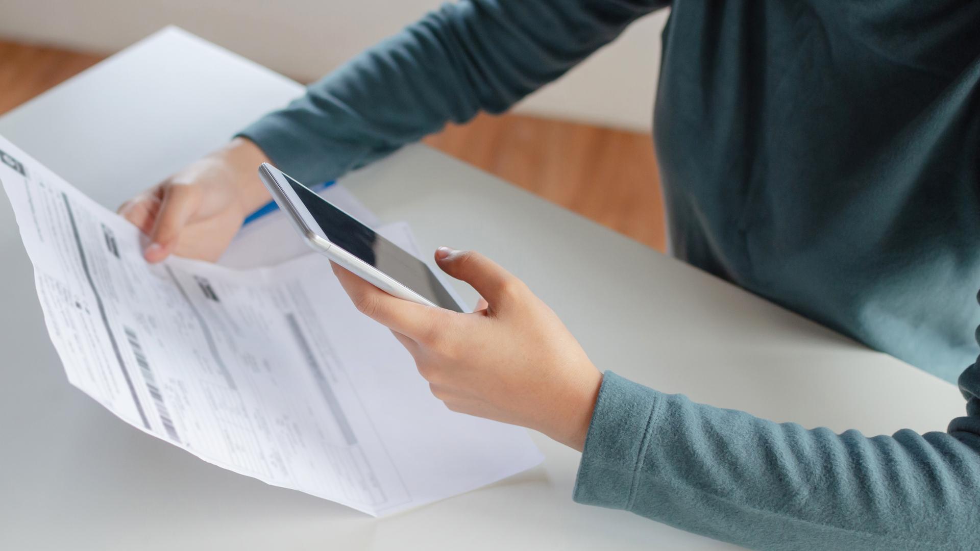 En ung kvinnas händer använder en smartphone för att skanna och betala räkningar online.