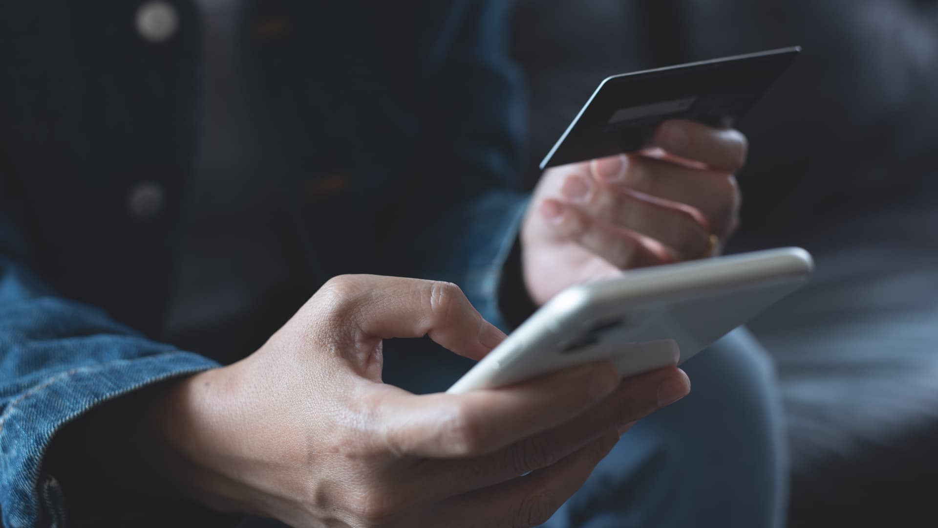En ung kvinnas händer håller ett bankkort i ena handen och en smartphone i den andra.