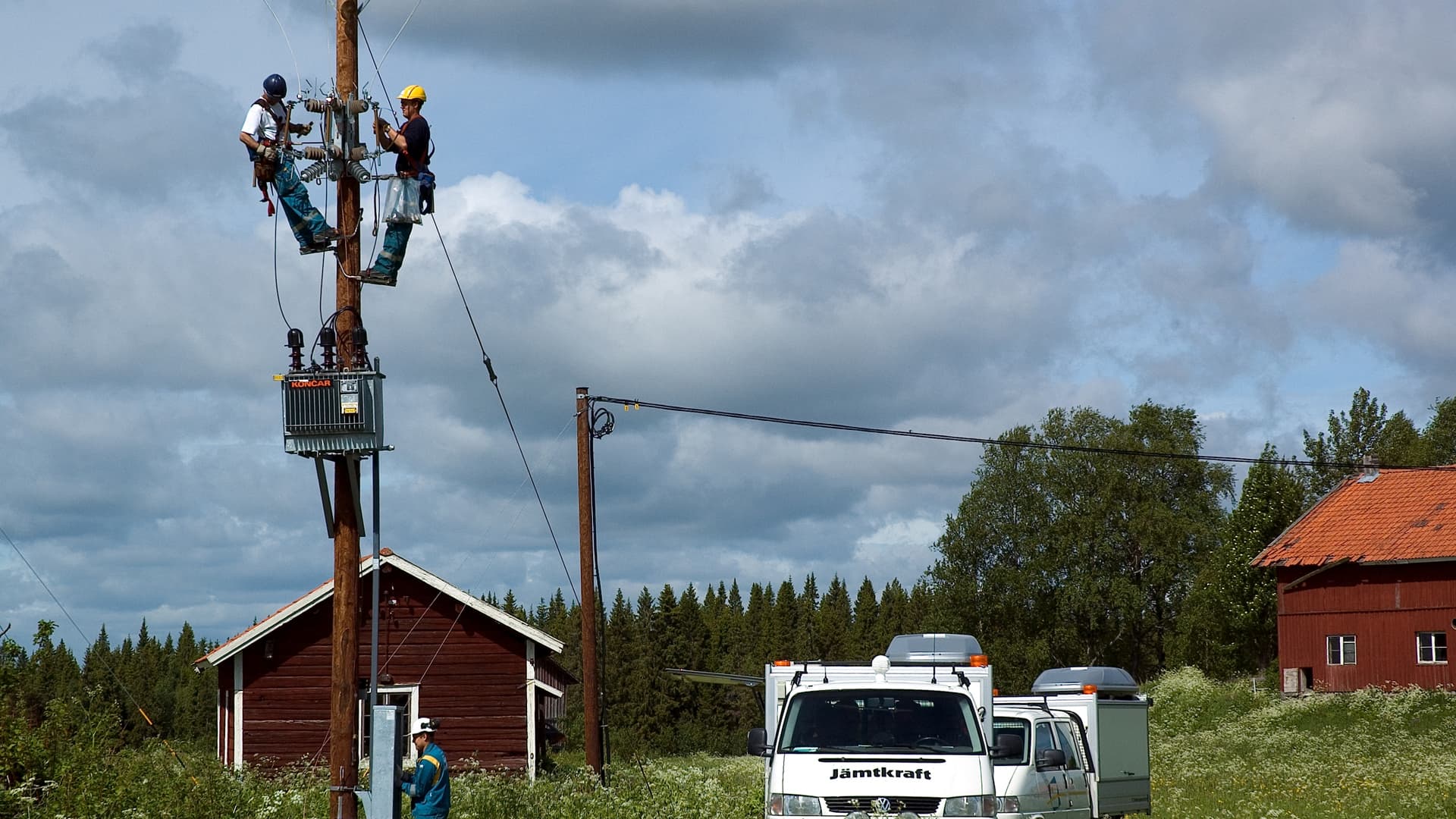 Två eltekniker jobbar med elledning uppe i en stolpe