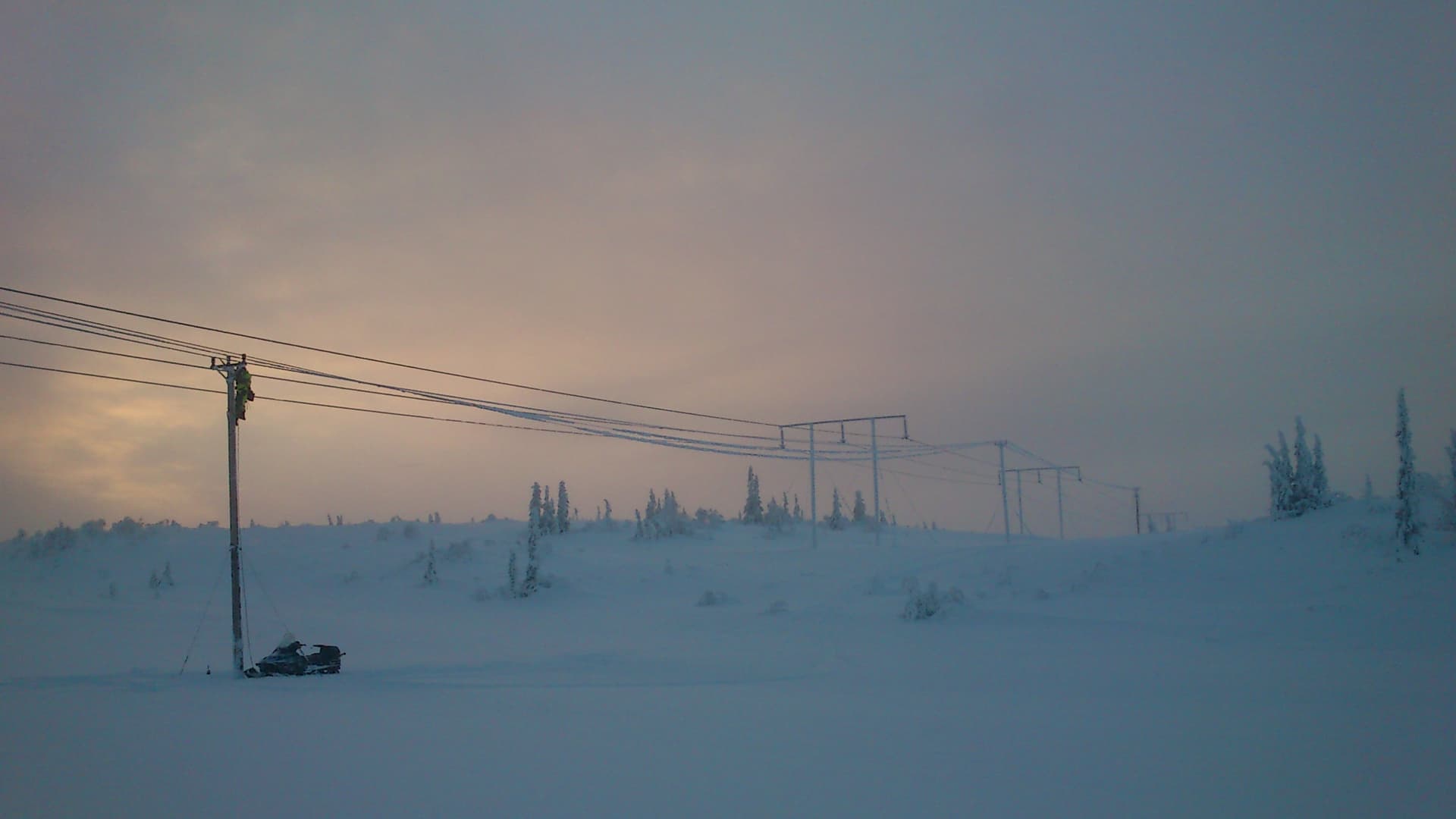 En man med skoter reparerar en elledning långt ute på fjället