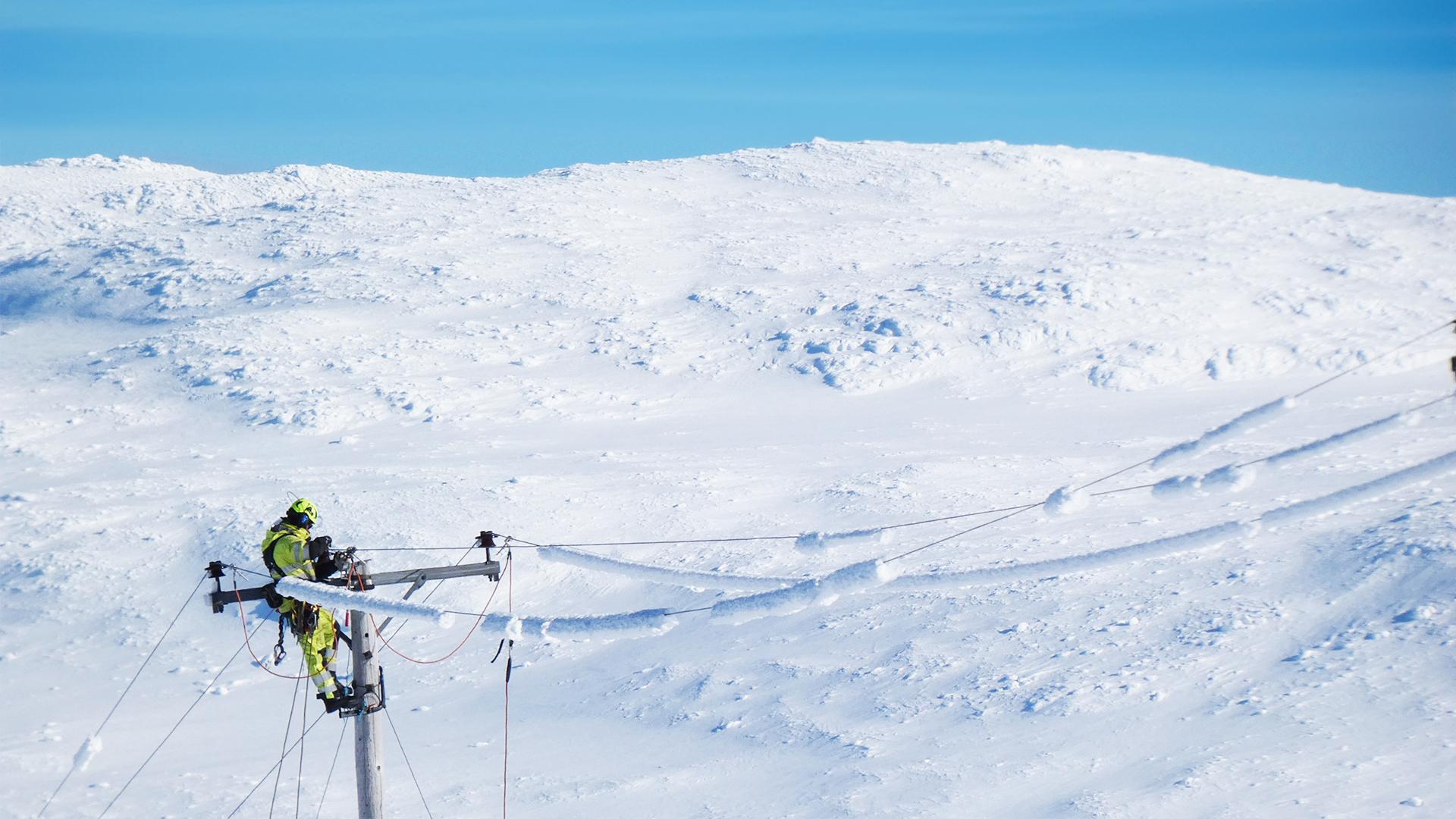 En medarbetare på Jämtkraft lagar elnät på hög höjd en solig vinterdag.