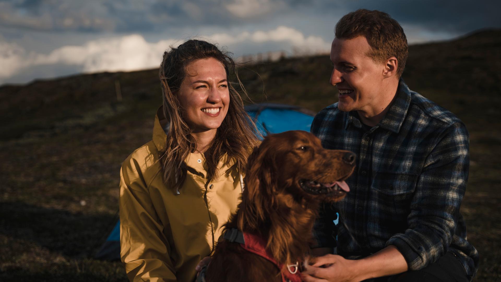 En kvinna och en man sitter på ett fjäll med en hund emellan sig.