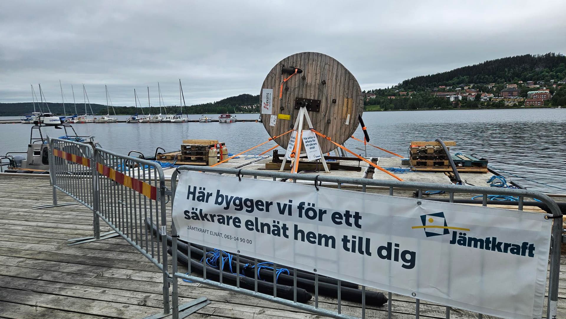 Pråm som ligger i en sjö samt en skylt med texten "Här bygger vi för ett säkrare elnät hem till dig".