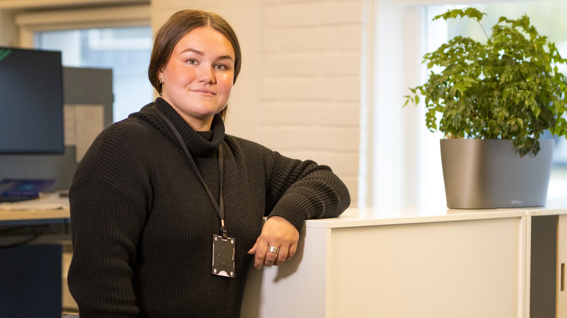 Rebecka Brink, en ung kvinna i svart tröja står vid ett bord och tittar in i kameran.