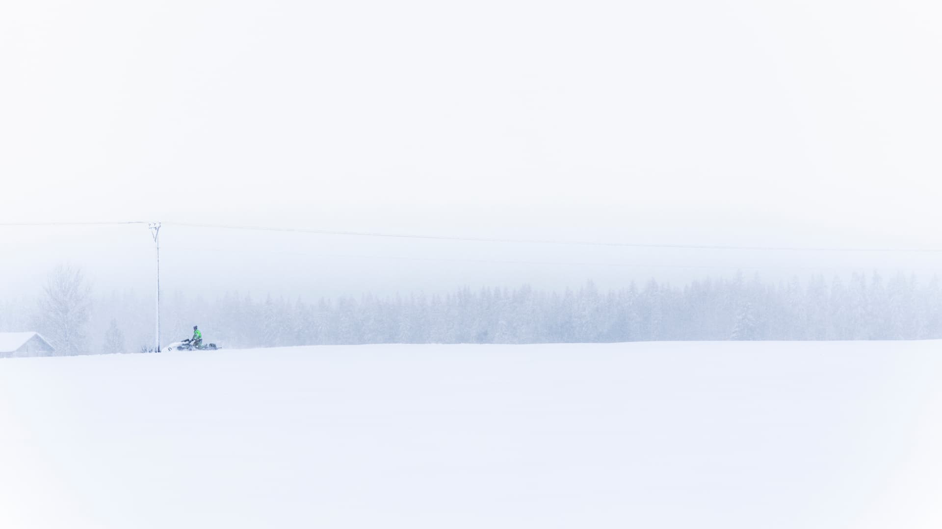 En skoter syns på håll vid en elledning i ett vitt och stormigt vinterlandskap.