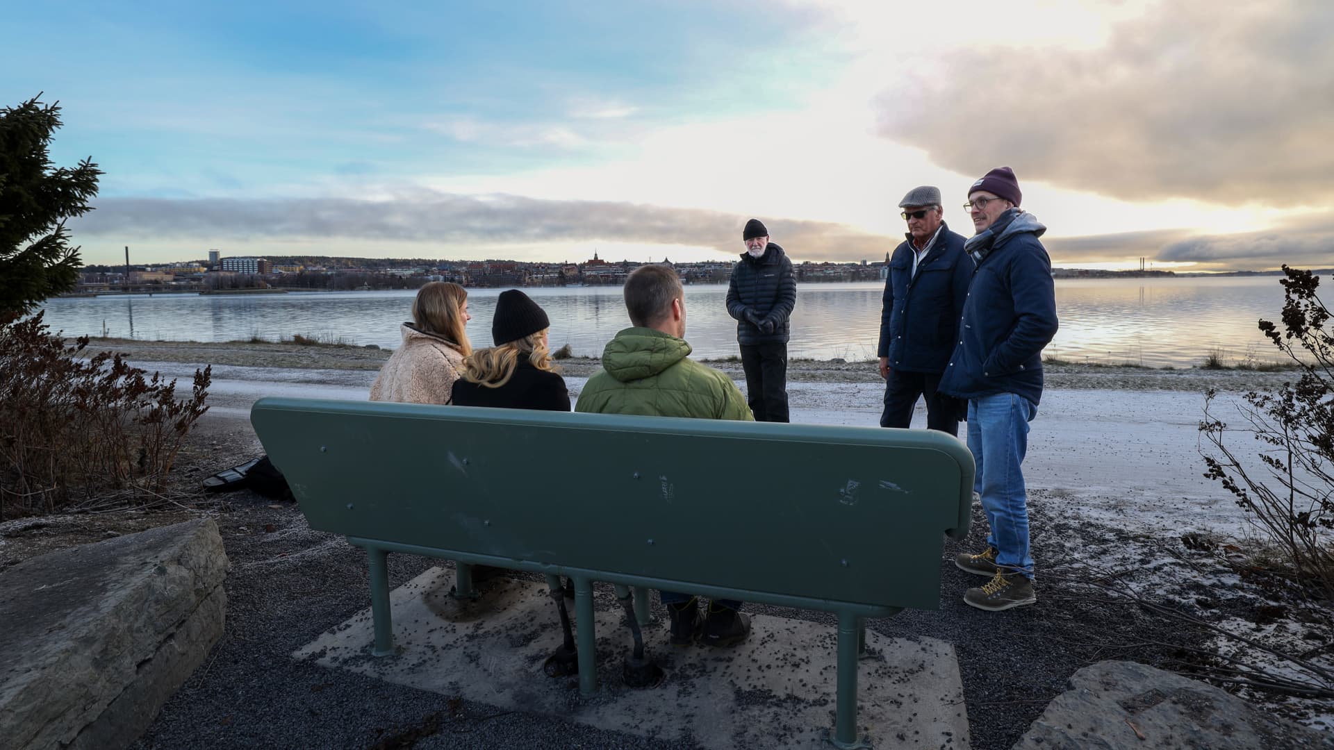 Flera personer sitter på en varm fjärrvärmebänk en kall vinterdag.