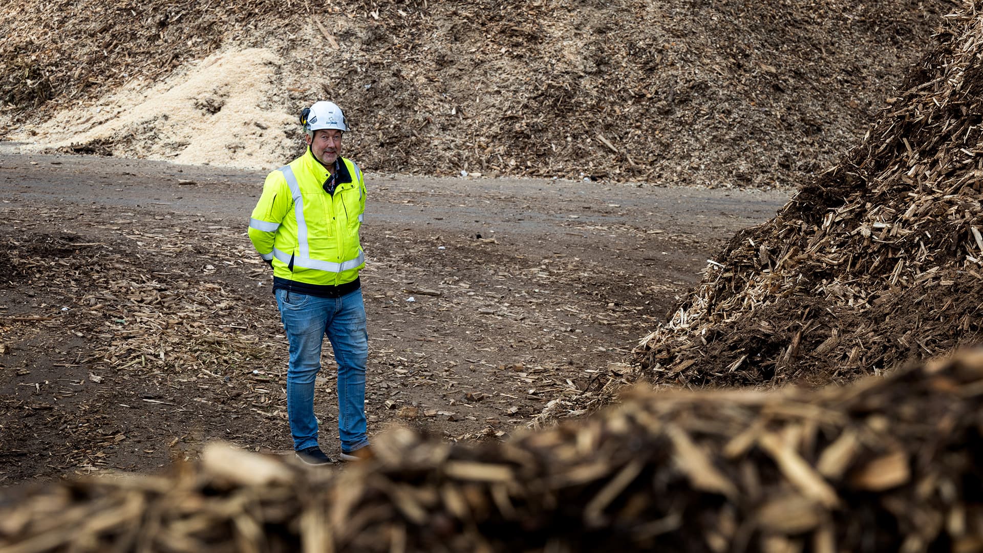 Hans Eriksson, chef för bränsleinköp på Jämtkraft, står i arbetskläder vid högar av grot.