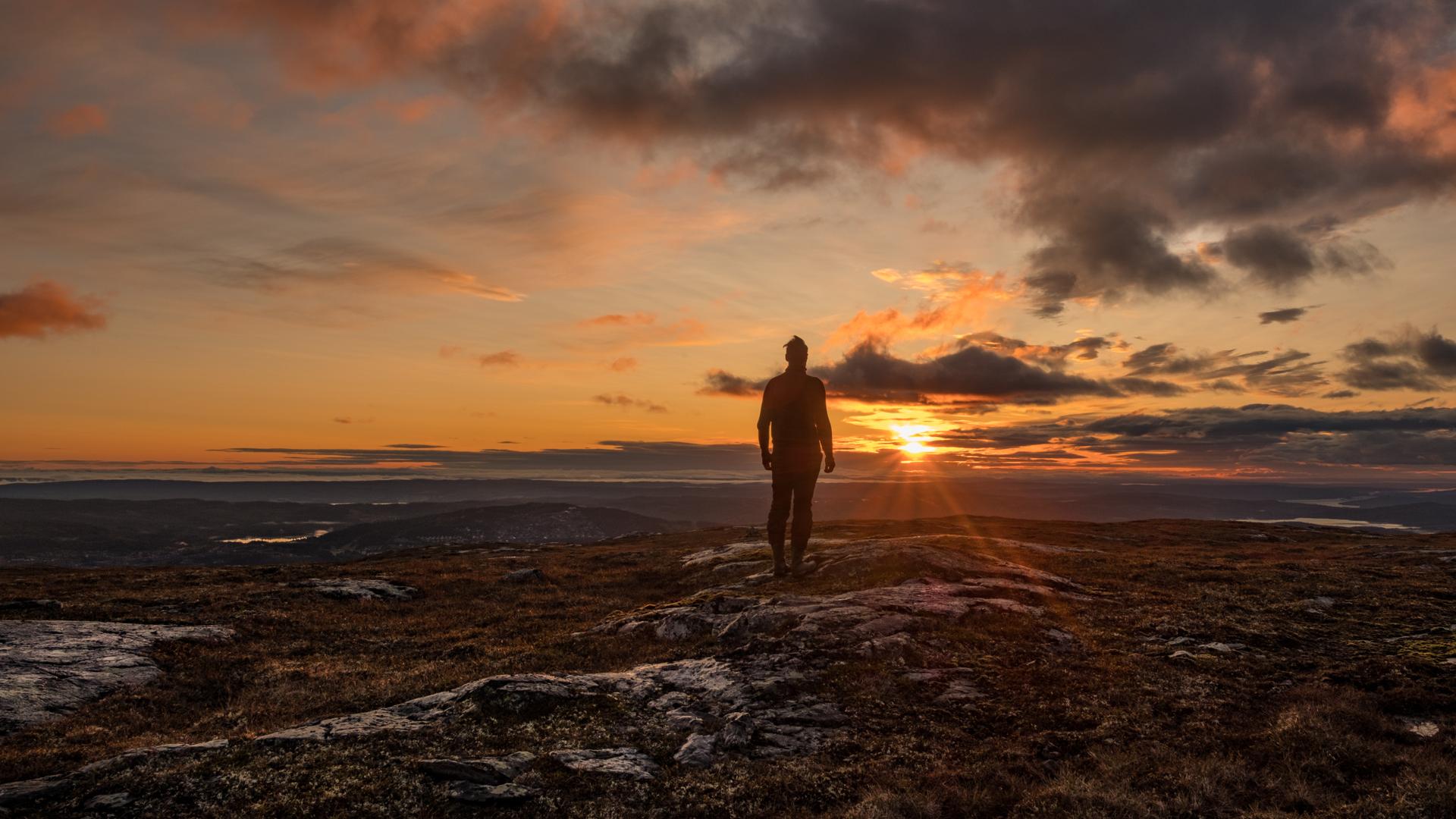 En person står i motljus i solnedgång på ett fjäll i Åre.