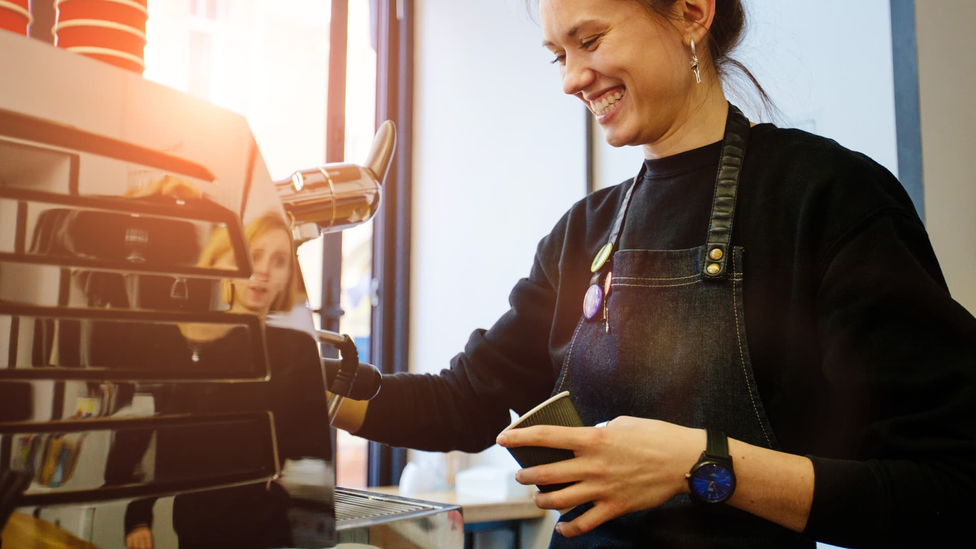 En kvinna ler och serverar kaffe i kassan på ett kafé