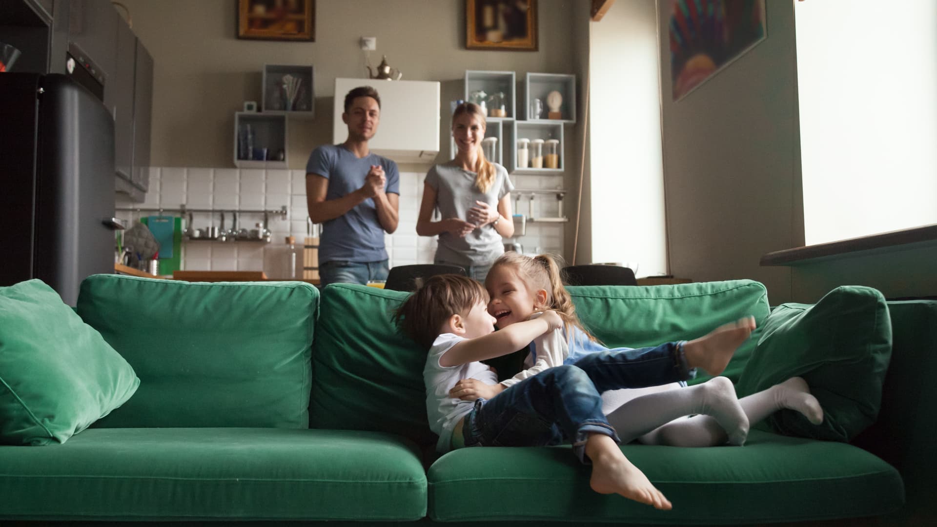 Två barn busar i en grön soffa. Bakom soffan står en man och en kvinna.