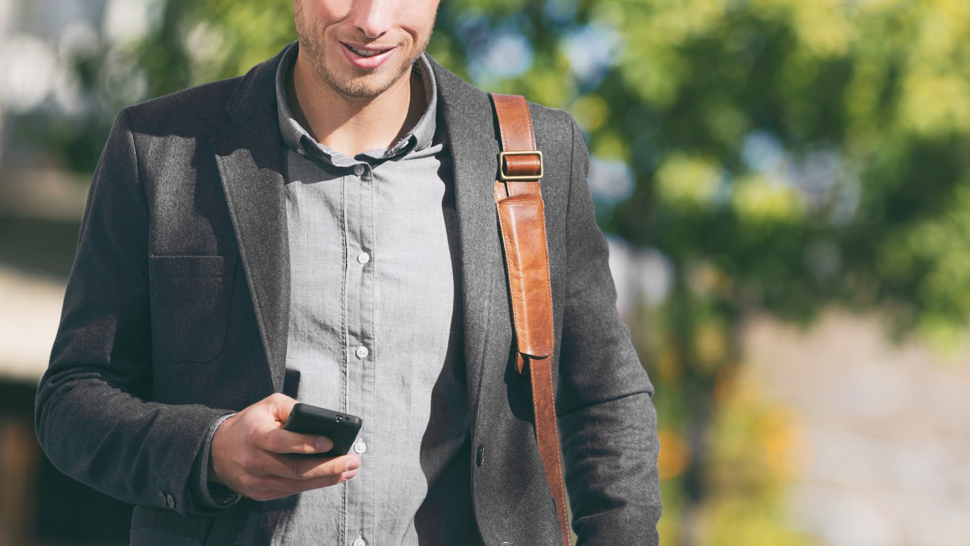 En man går med väska över axel och mobiltelefon i handen