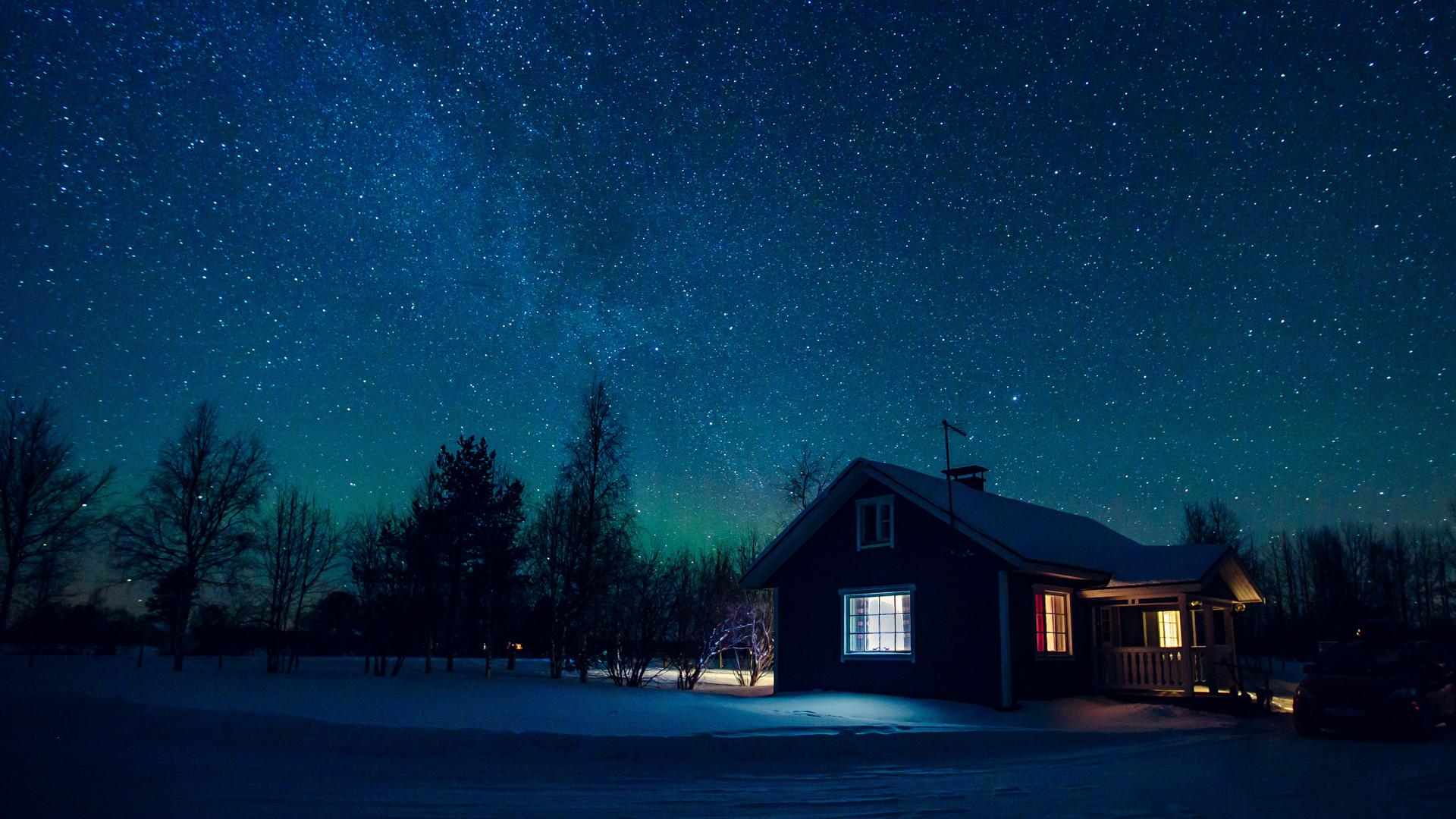 Ett litet, ensamt hus i vinternatt med stjärnklar himmel