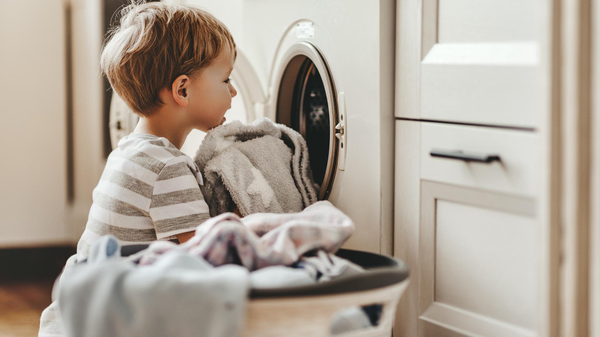 Ett barn lägger kläder i en tvättmaskin