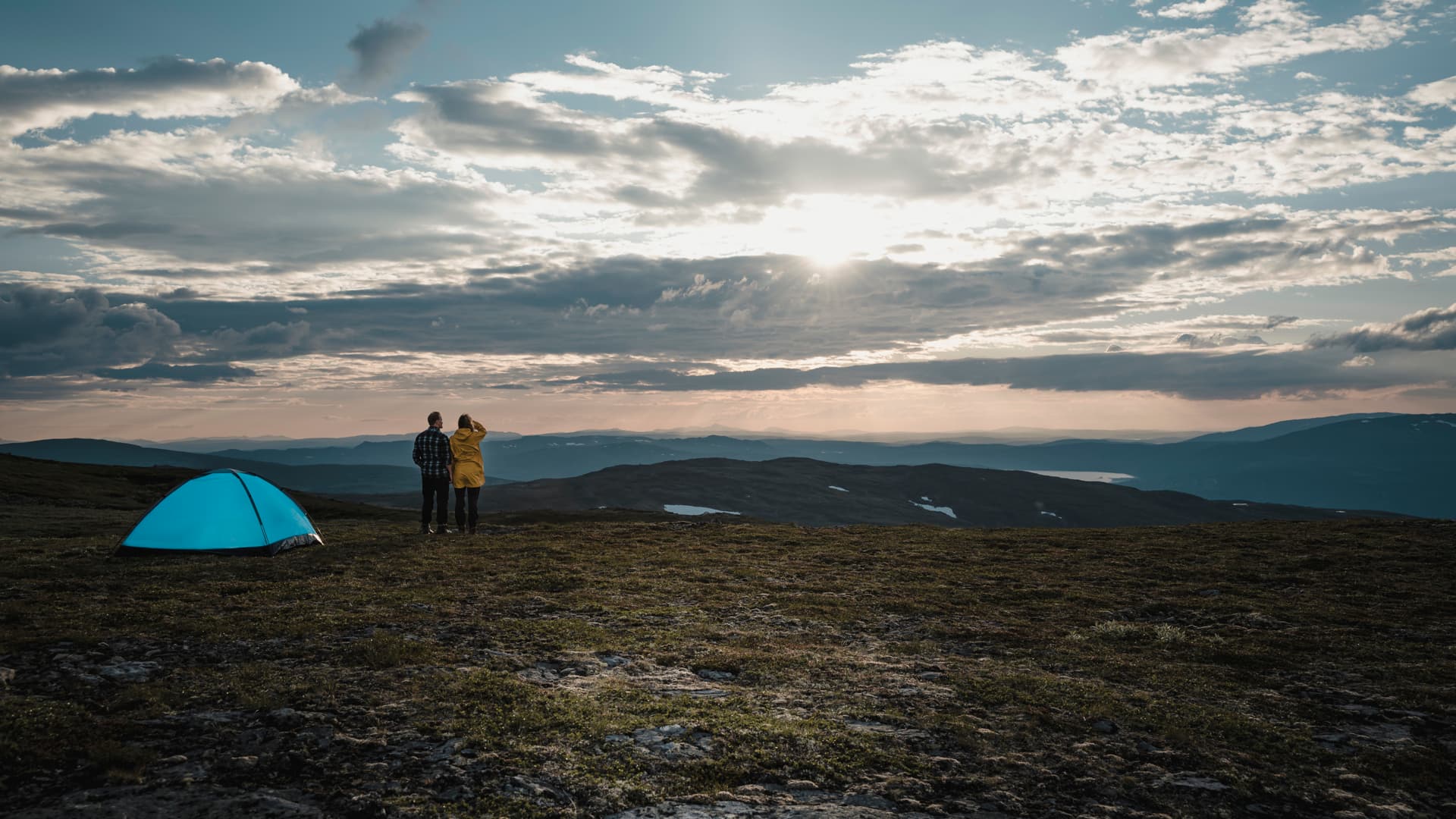 Ett par ser ut över fjällen bredvid ett blått tält