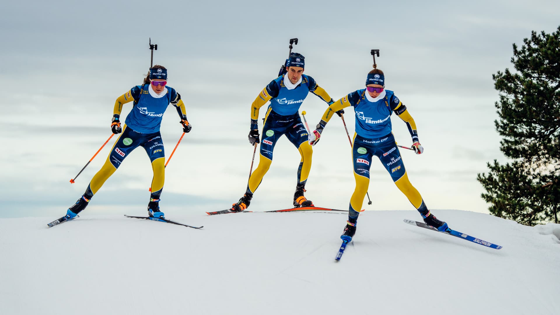 Tre skidskyttar åker skidor nerför en snöig backe.