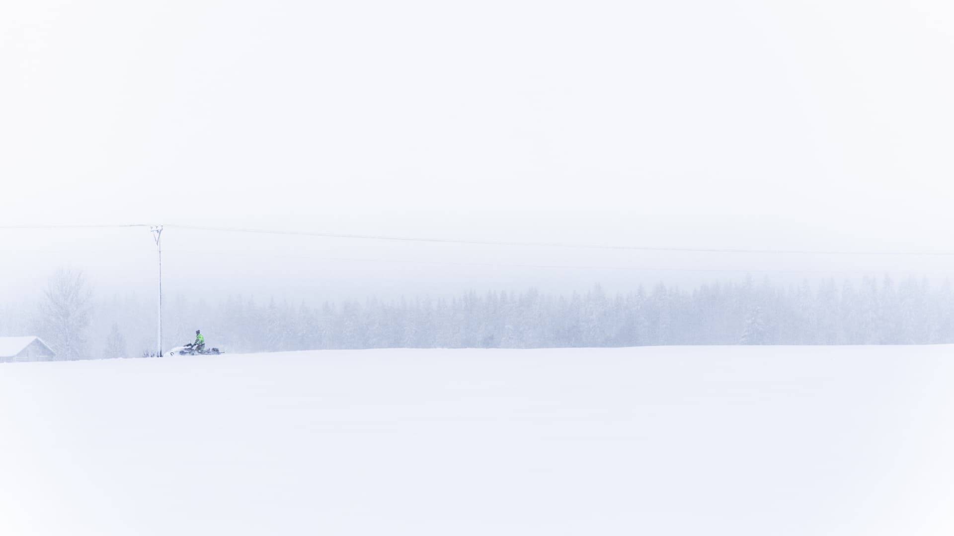 En skoter syns på håll vid en elledning i ett vitt och stormigt vinterlandskap.
